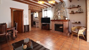 A cozy living room with a fireplace, wooden beams, a television, and a dining area.