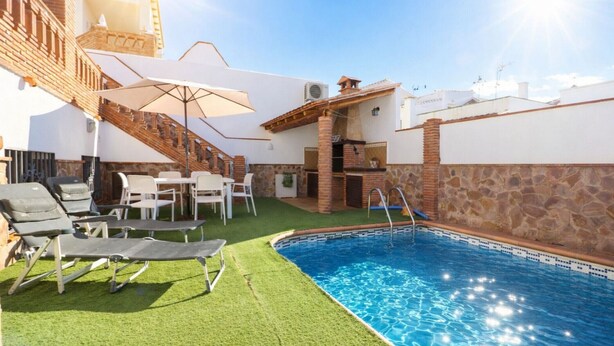 A swimming pool with a brick deck, surrounded by artificial grass and lounge chairs.