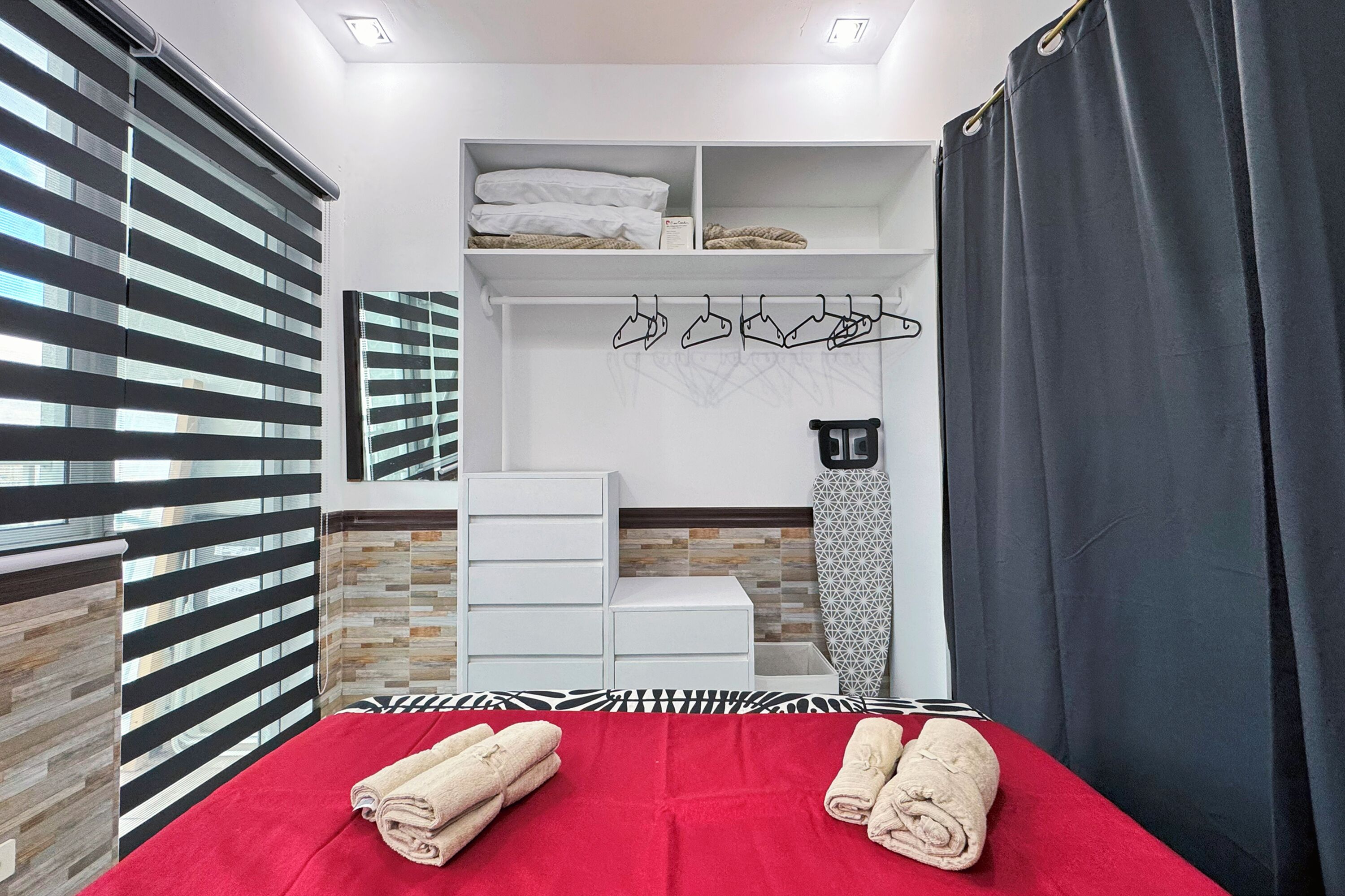 A hotel room with a bed, a wardrobe, a mirror, and a shelf with towels and hangers.