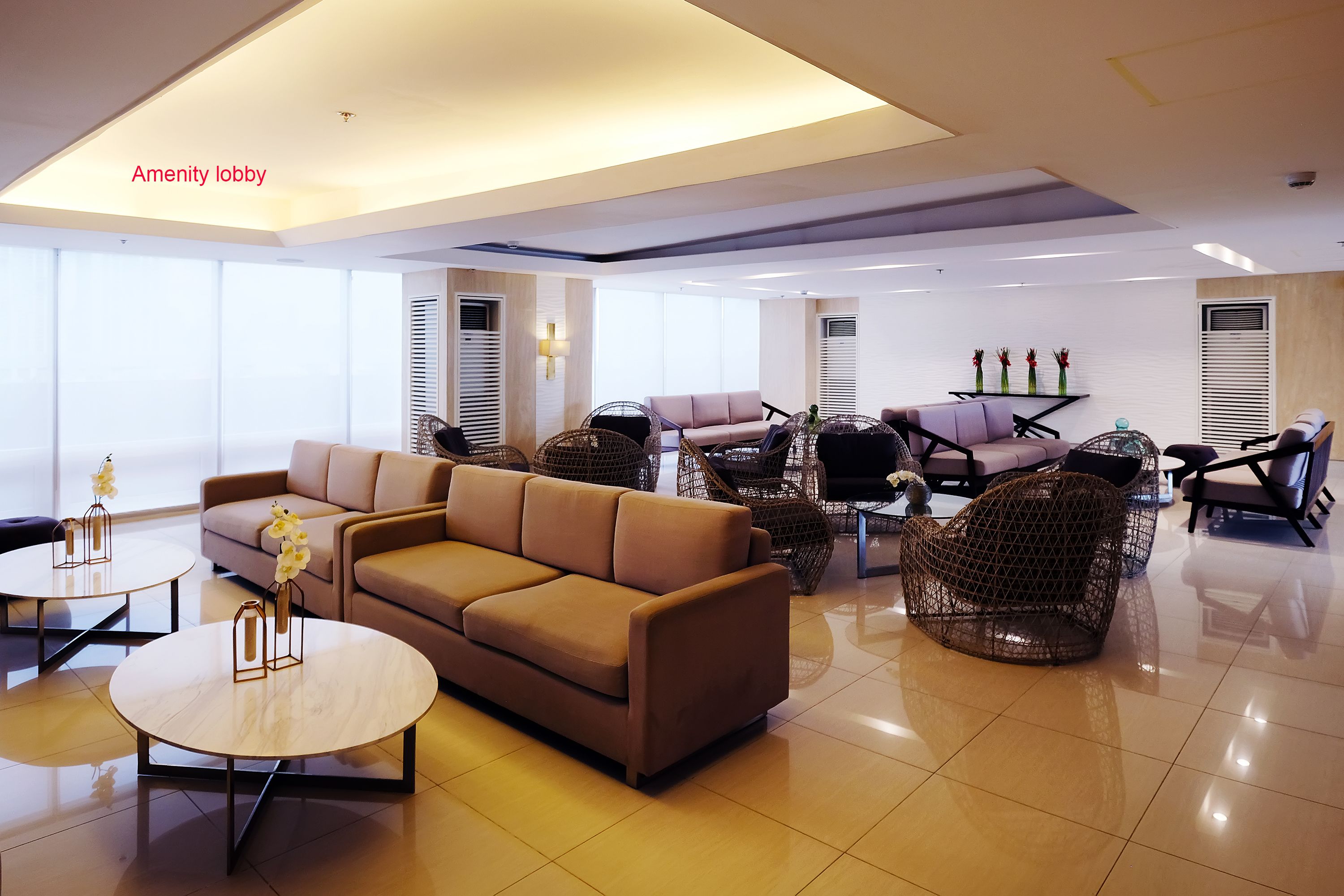 A modern amenity lobby with a beige sofa, wicker chairs, and a round coffee table.