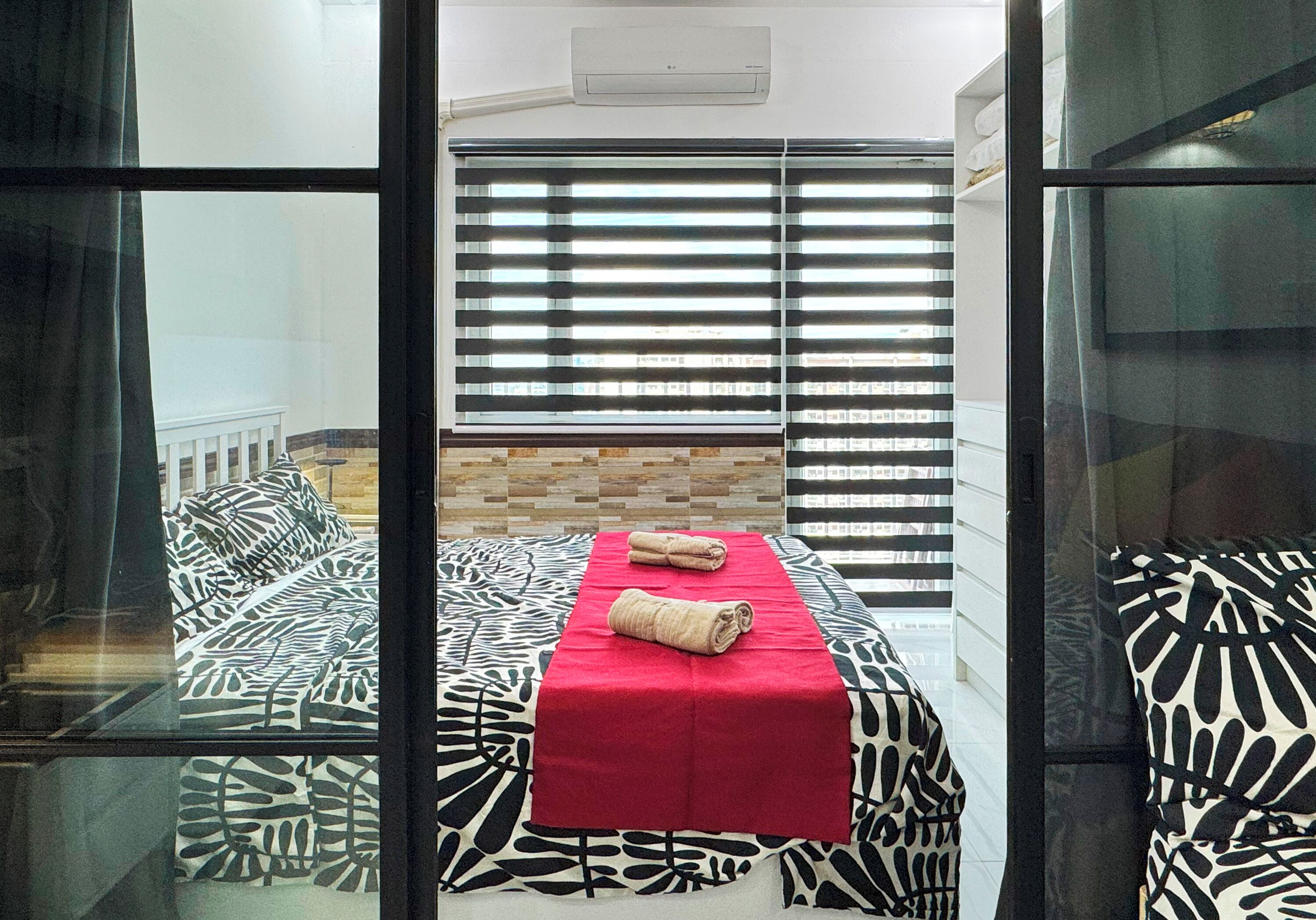 Ein Zimmer mit einem Bett, einer roten Decke und einem Fenster mit Jalousien.