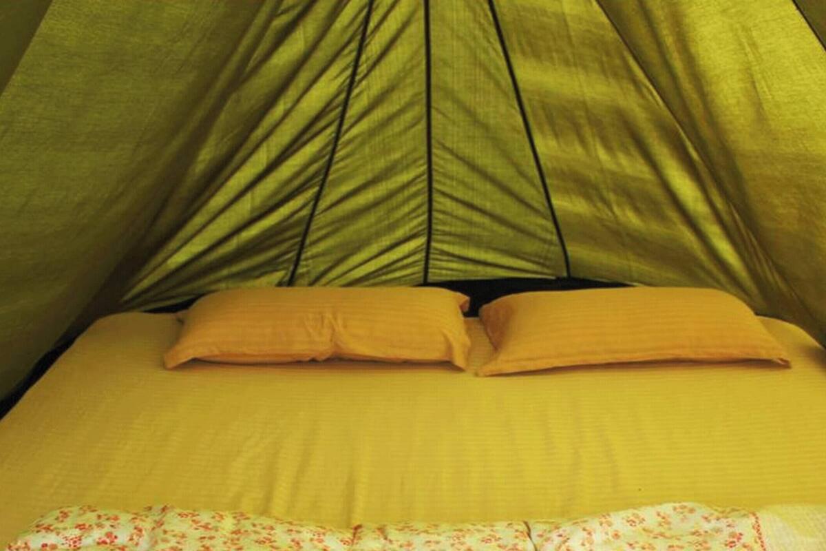 Une tente équipée d’un lit, d’oreillers et d’une couverture à motifs floraux.