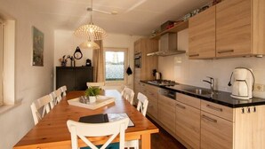 A modern kitchen with wooden cabinets, a dining table with chairs, a chandelier, and a view of the outdoors. - Duinweg 12 comfortable luxury holiday villa near beach (Renesse)