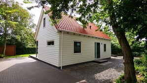 A small, single-story house with a red-tiled roof, white siding, and a gravel driveway. - Duinweg 12 comfortable luxury holiday villa near beach (Renesse)
