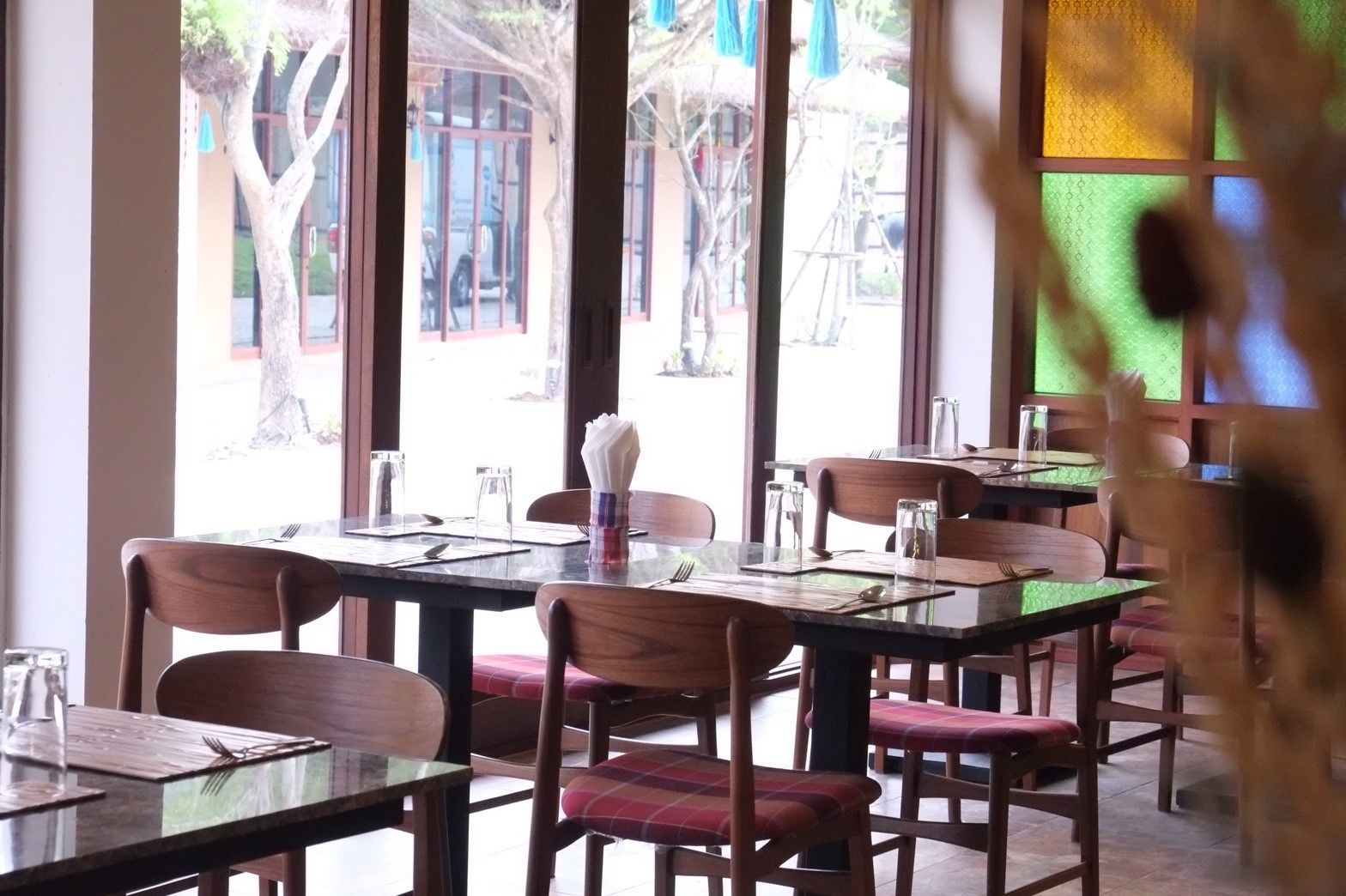 An indoor dining area with wooden tables and chairs, clear glass windows, and a view of the outside.
