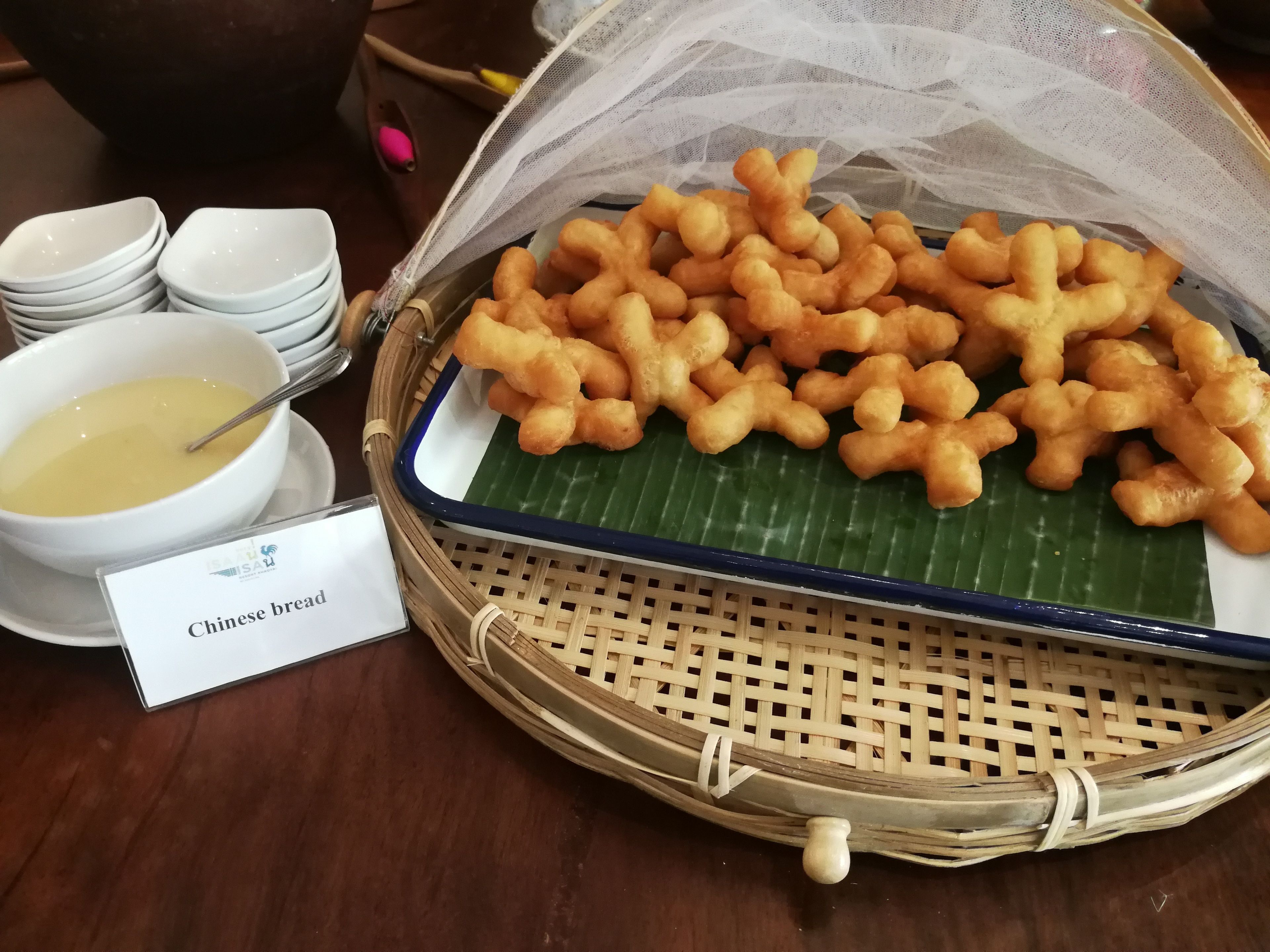 Una cesta de pan chino sobre una mesa con un cartel, tazones de sopa y un posavasos.