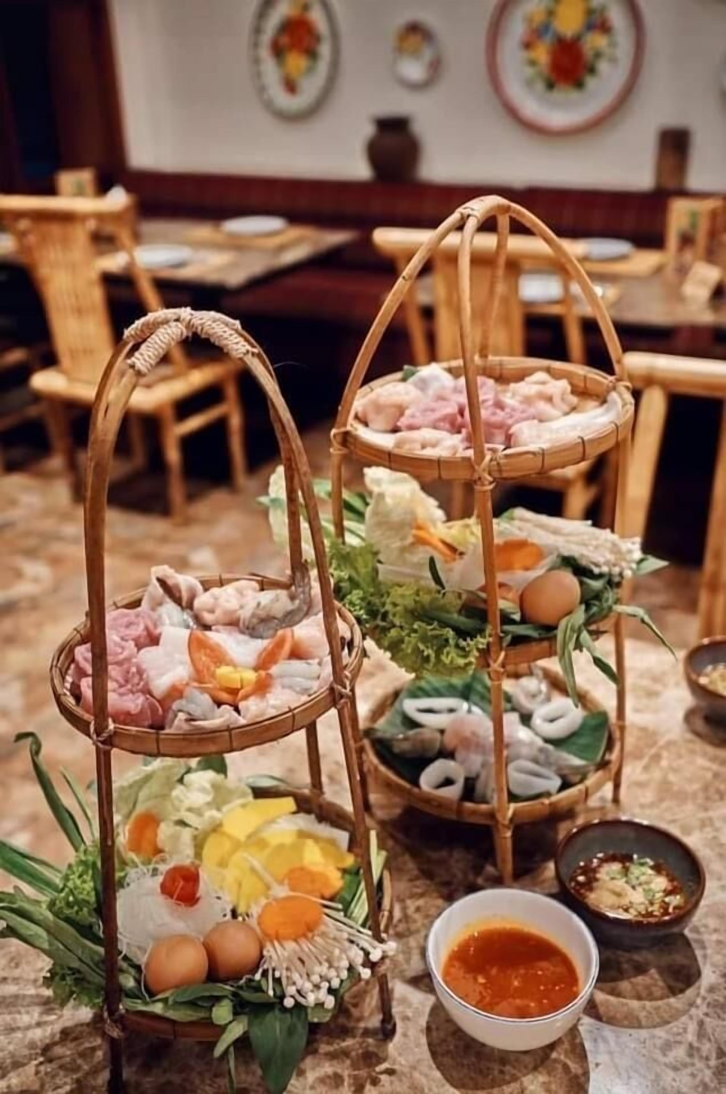 A three-tiered bamboo stand with various food items and a small bowl of sauce.
