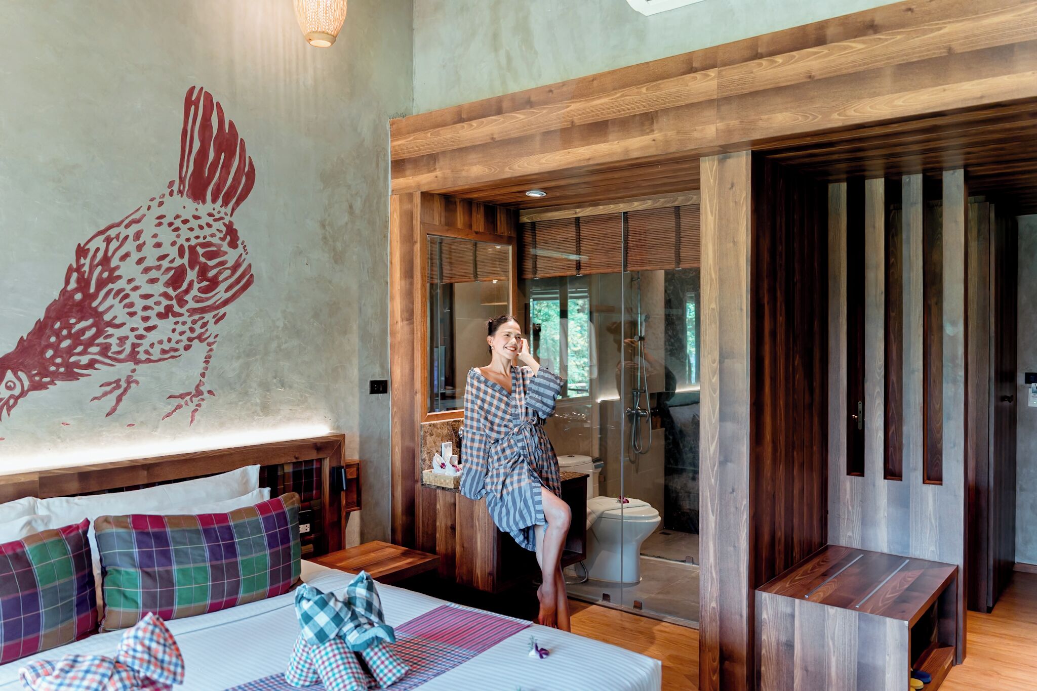 A modern hotel room with a large bed, a wooden headboard, a bathroom with a glass shower, and a wall mural.