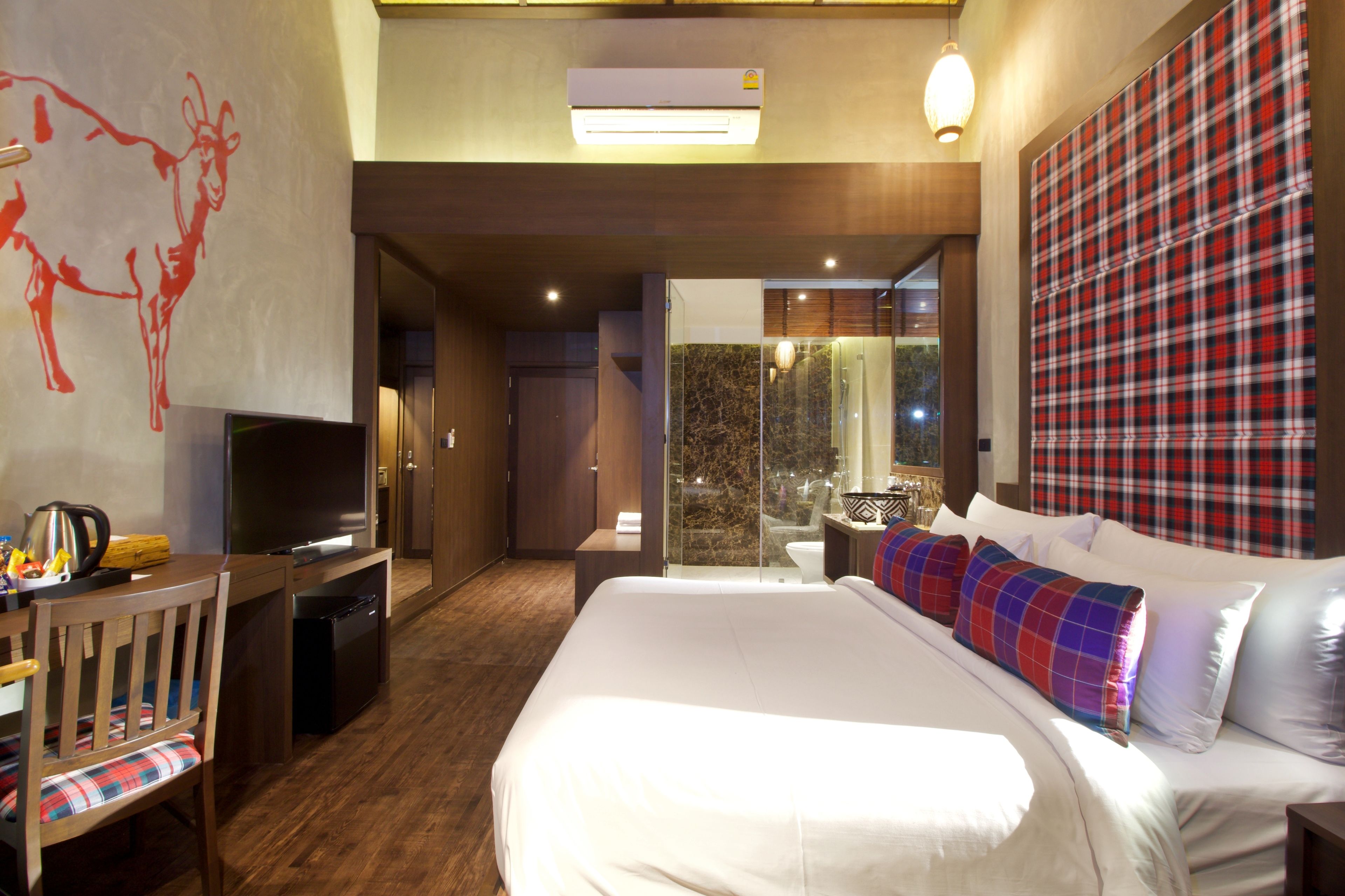 Quarto de hotel com uma cama grande, uma secretária com televisão, área de chuveiro e vista para o exterior.