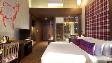 Quarto de hotel com uma cama grande, uma secretária com televisão, área de chuveiro e vista para o exterior.