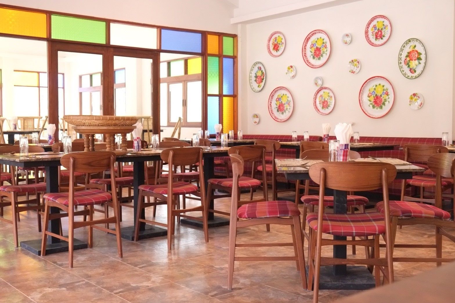 Un restaurante con mesas y sillas de madera, suelo de baldosas y una pared decorada con platos.