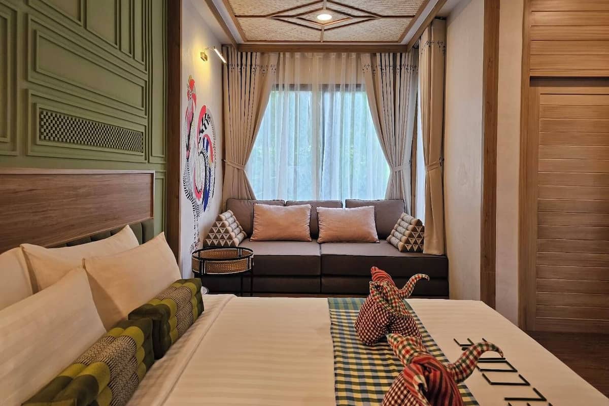 A hotel room with a large bed, a sofa bed, a decorative wall, and a view of the outdoors through sheer curtains.