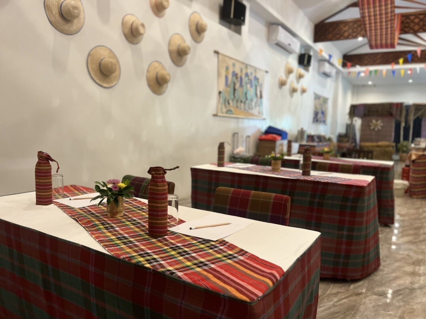 A restaurant with plaid tablecloths, wooden chairs, and a variety of wall decorations including hats and a painting.