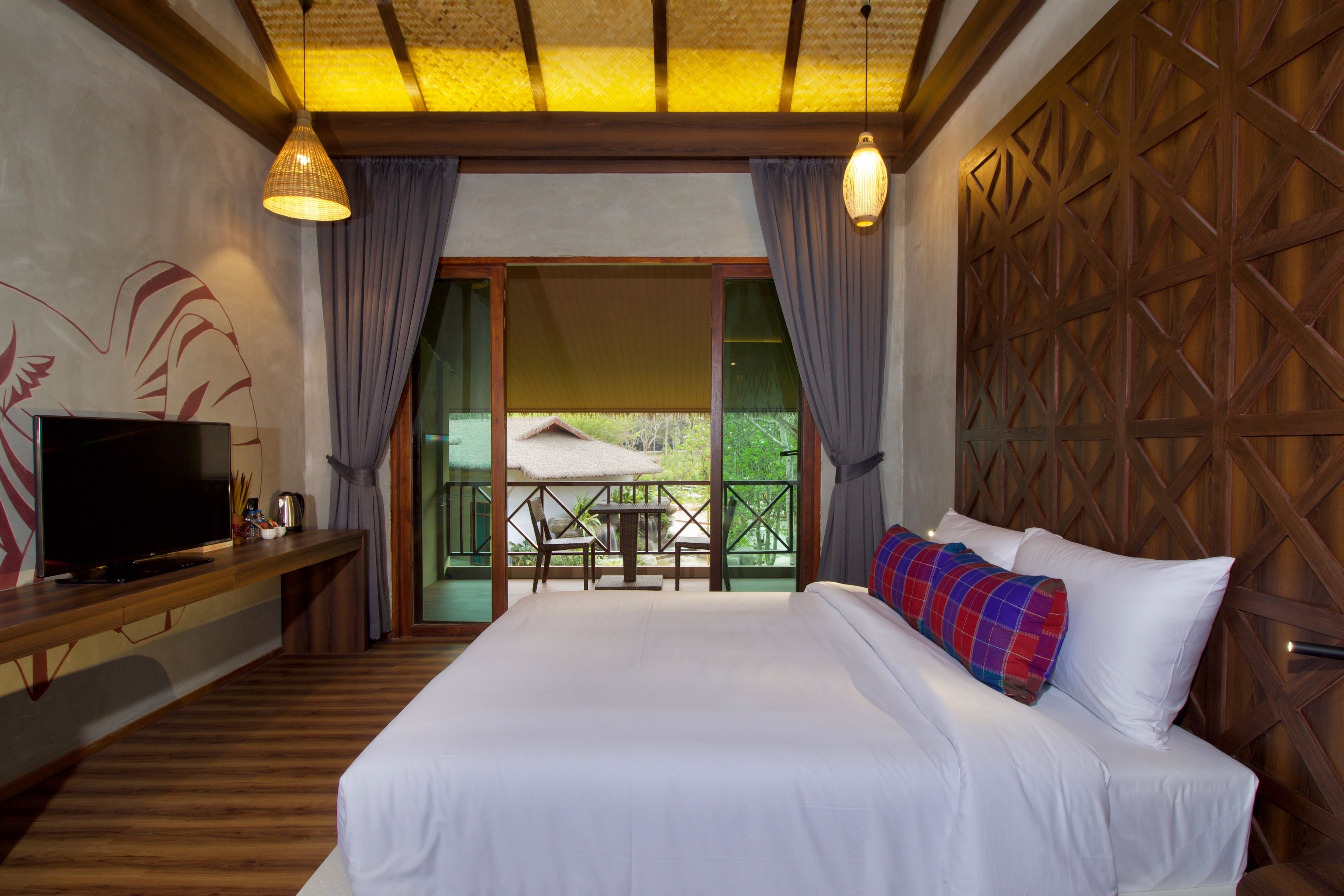 A hotel room with a large bed, a TV on a wooden console, a balcony with a table and chairs, and a wooden wall panel.