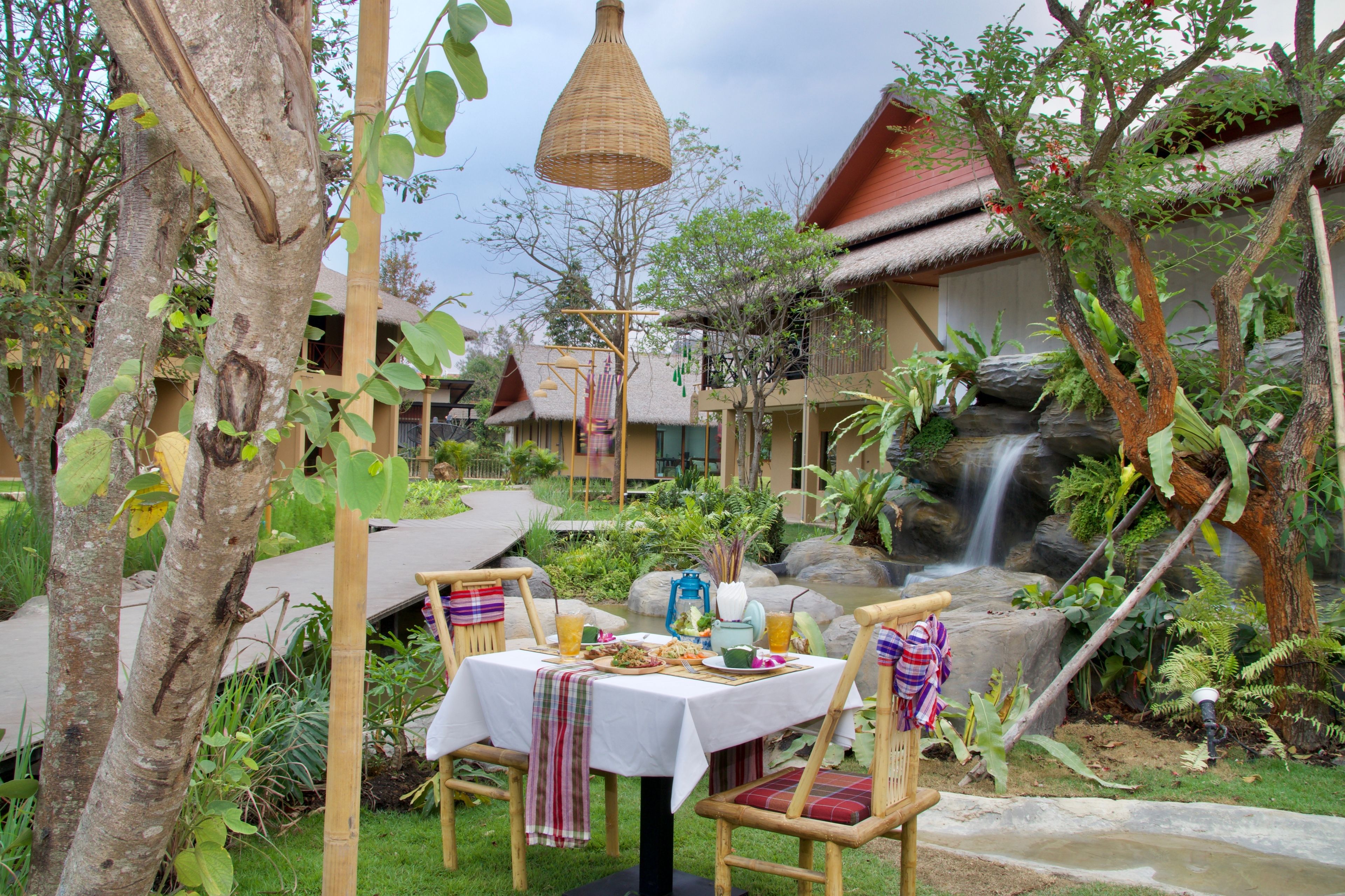 A dining area with a table set for two, surrounded by natural scenery including trees and a waterfall.