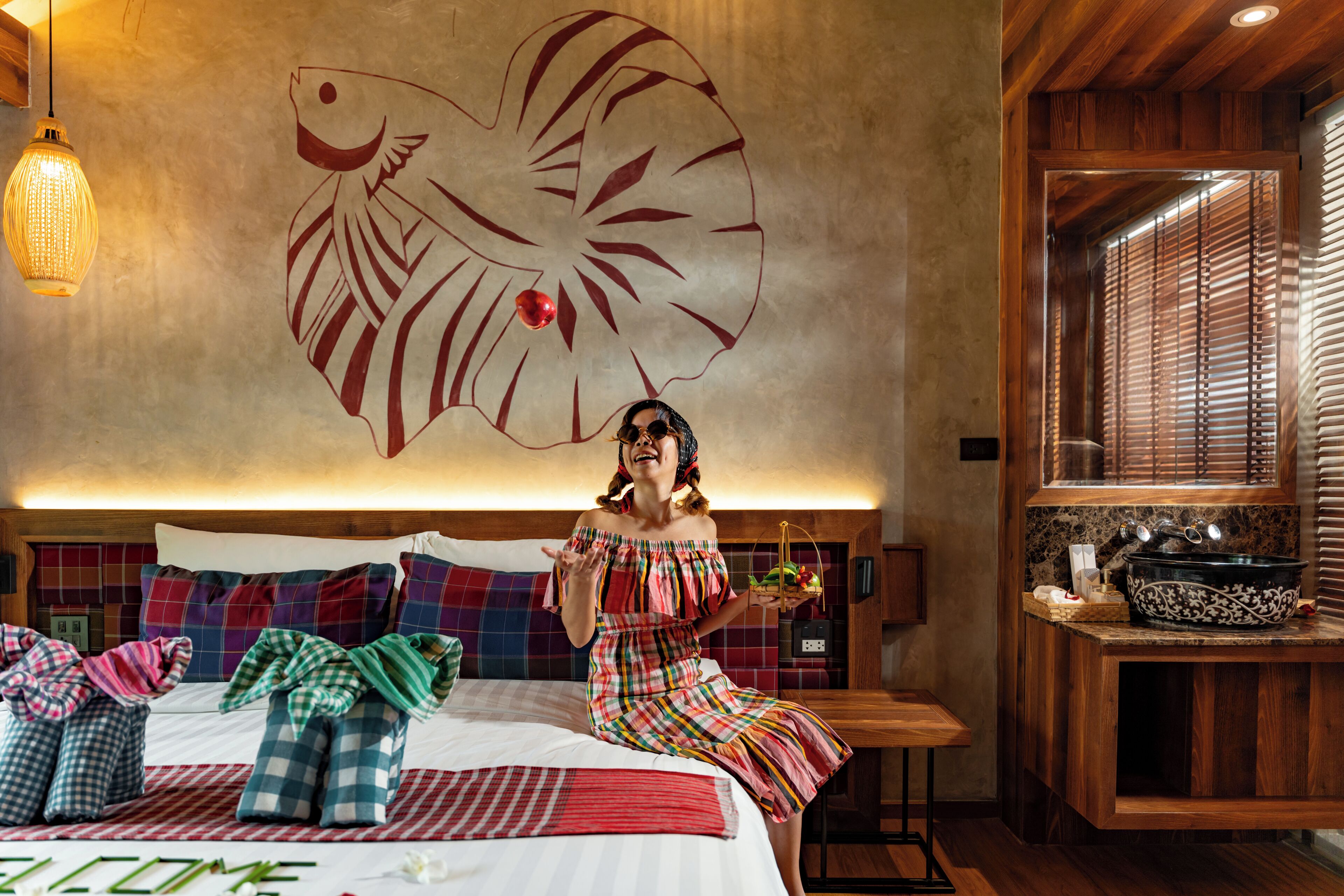 A hotel room with a large bed, a wooden headboard, a wall mural, a small table, and a window with blinds.