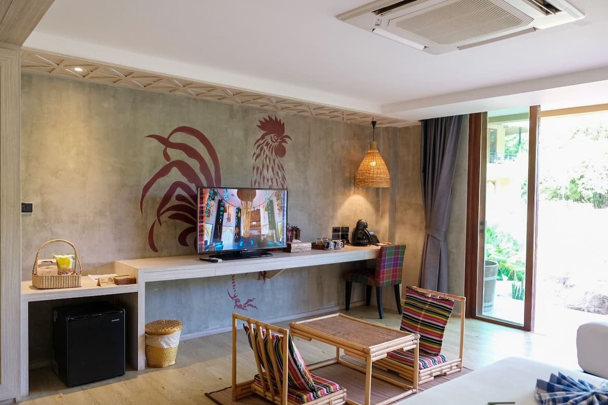 A modern living room with a flat-screen TV, wicker furniture, and a large window with a view of greenery.