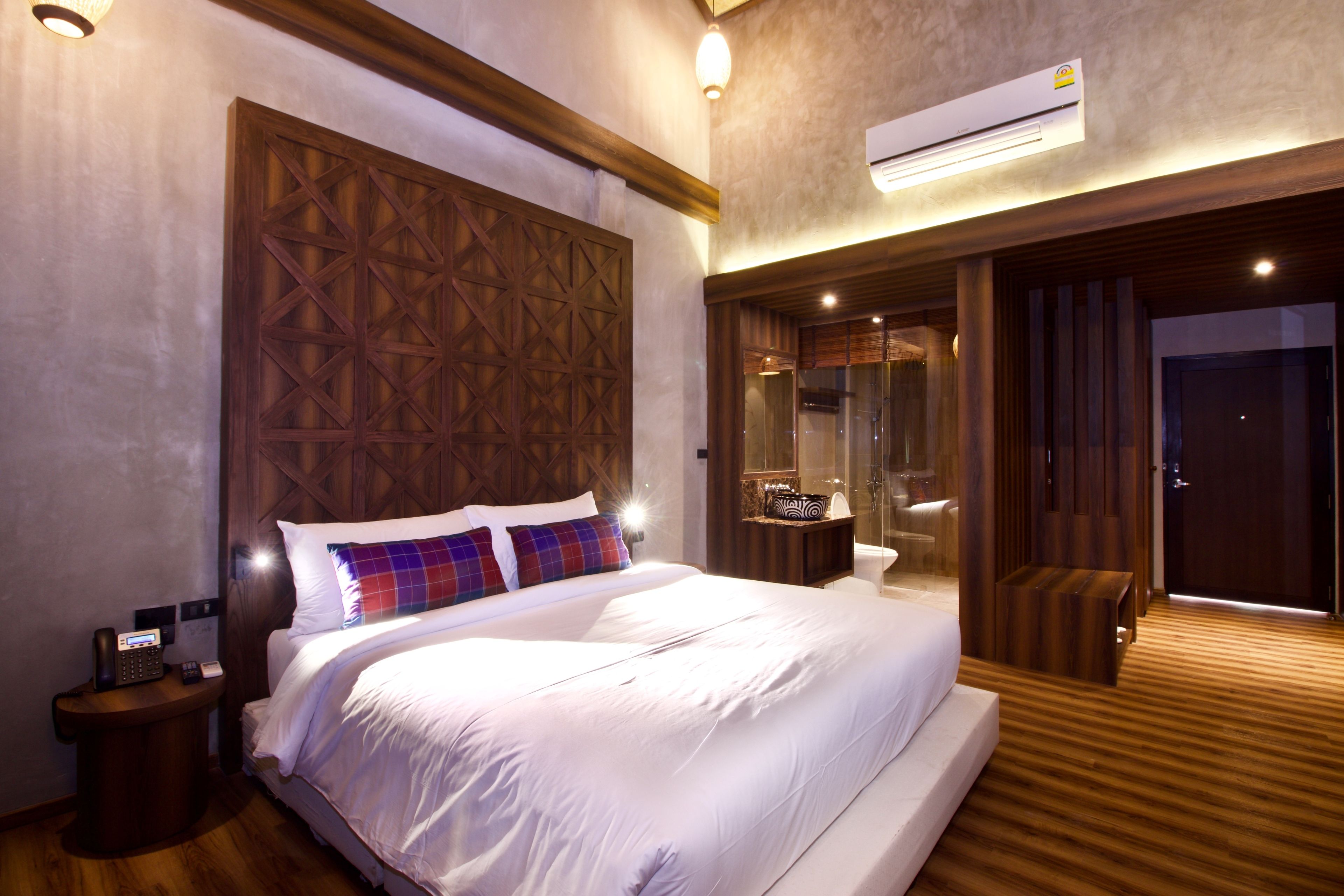 Une chambre d’hôtel moderne dotée d’un grand lit, d’une tête de lit en bois, d’une salle de bain avec une douche en verre et d’un climatiseur.