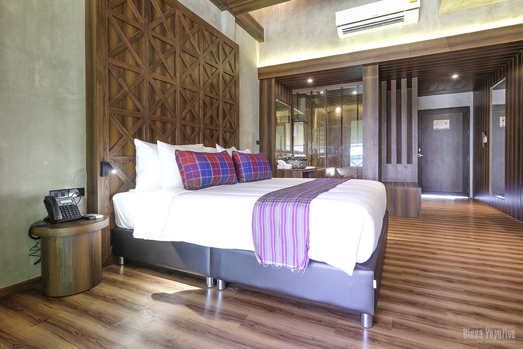 Une chambre d’hôtel moderne avec un grand lit, une tête de lit en bois, un téléphone sur la table de chevet et un plancher en bois.