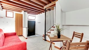 A modern living room with a red sofa, wooden dining table, and chairs. A staircase with a black railing leads to an upper floor. - Guggenheim Collection Venice Apartment (Venice)