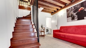 A staircase with wooden steps and black railings, leading to a room with a red sofa and a large framed picture on the wall. - Guggenheim Collection Venice Apartment (Venice)