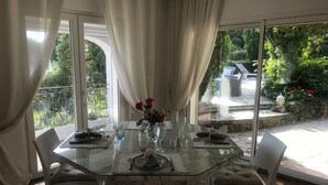 Une table à manger dressée pour deux personnes, avec un vase de fleurs, un verre d’eau et une bougie posés sur la table.