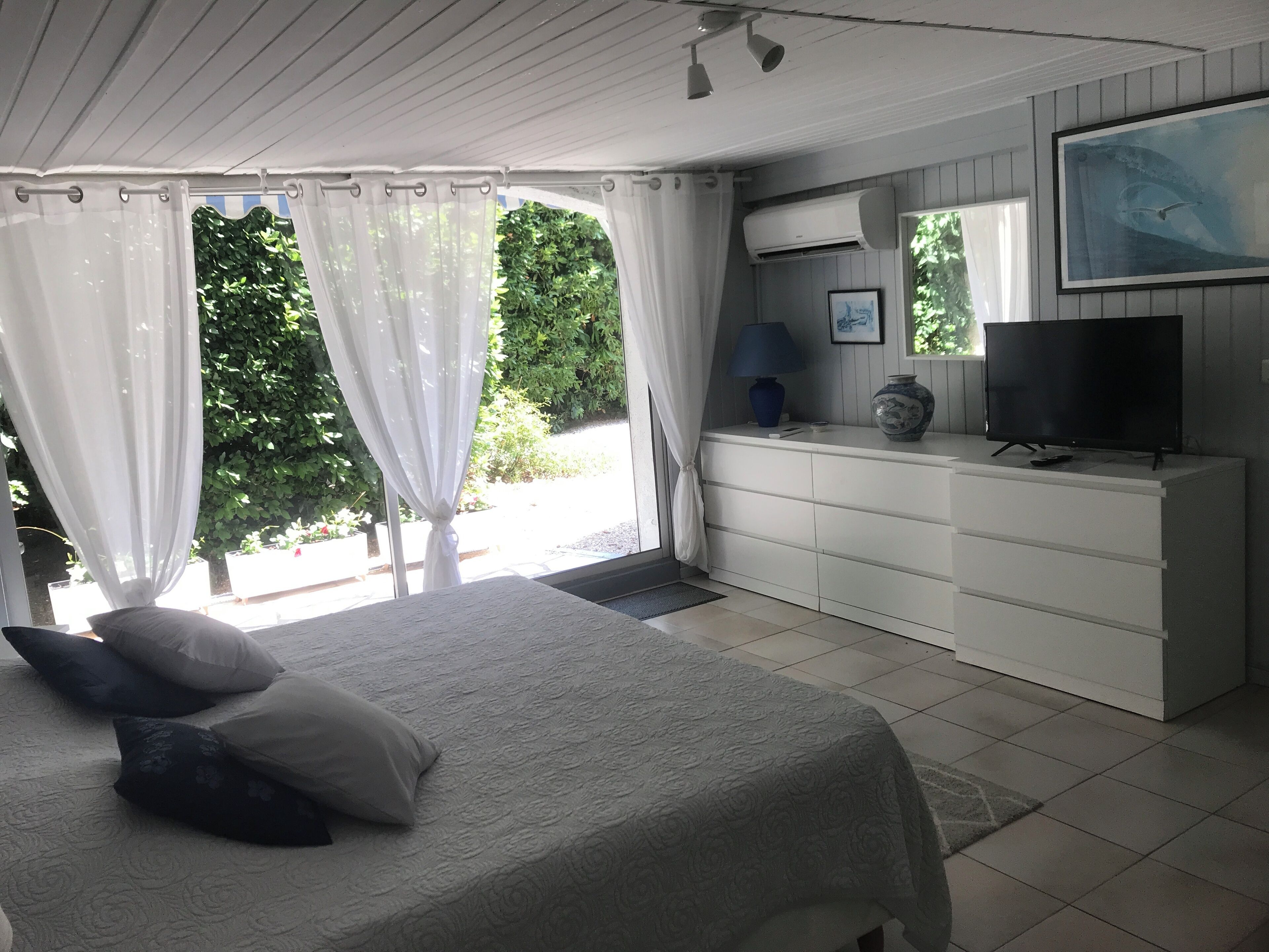 Une chambre à coucher avec un lit, une commode, un téléviseur et une fenêtre avec des rideaux.
