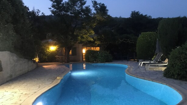 Une piscine à bord incurvé, entourée d’une terrasse en pierre et d’une haie.