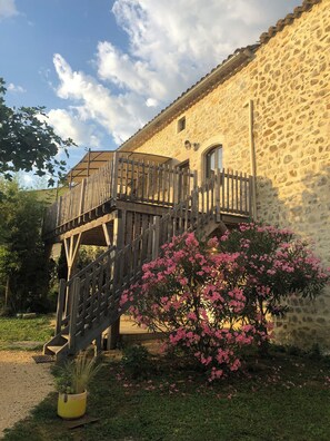 A stone building with a wooden balcony and a pink flowering bush in the foreground. - 18th century 3-star farmhouse - Private pool and garden (Lagorce)