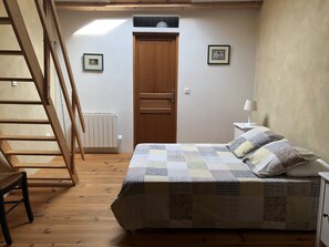 A bedroom with a wooden bed, a nightstand, a chair, a wooden ladder, a door, and a radiator. - 18th century 3-star farmhouse - Private pool and garden (Lagorce)
