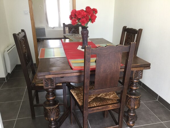 A dining table with six wooden chairs, a vase with red flowers, and a colorful placemat.