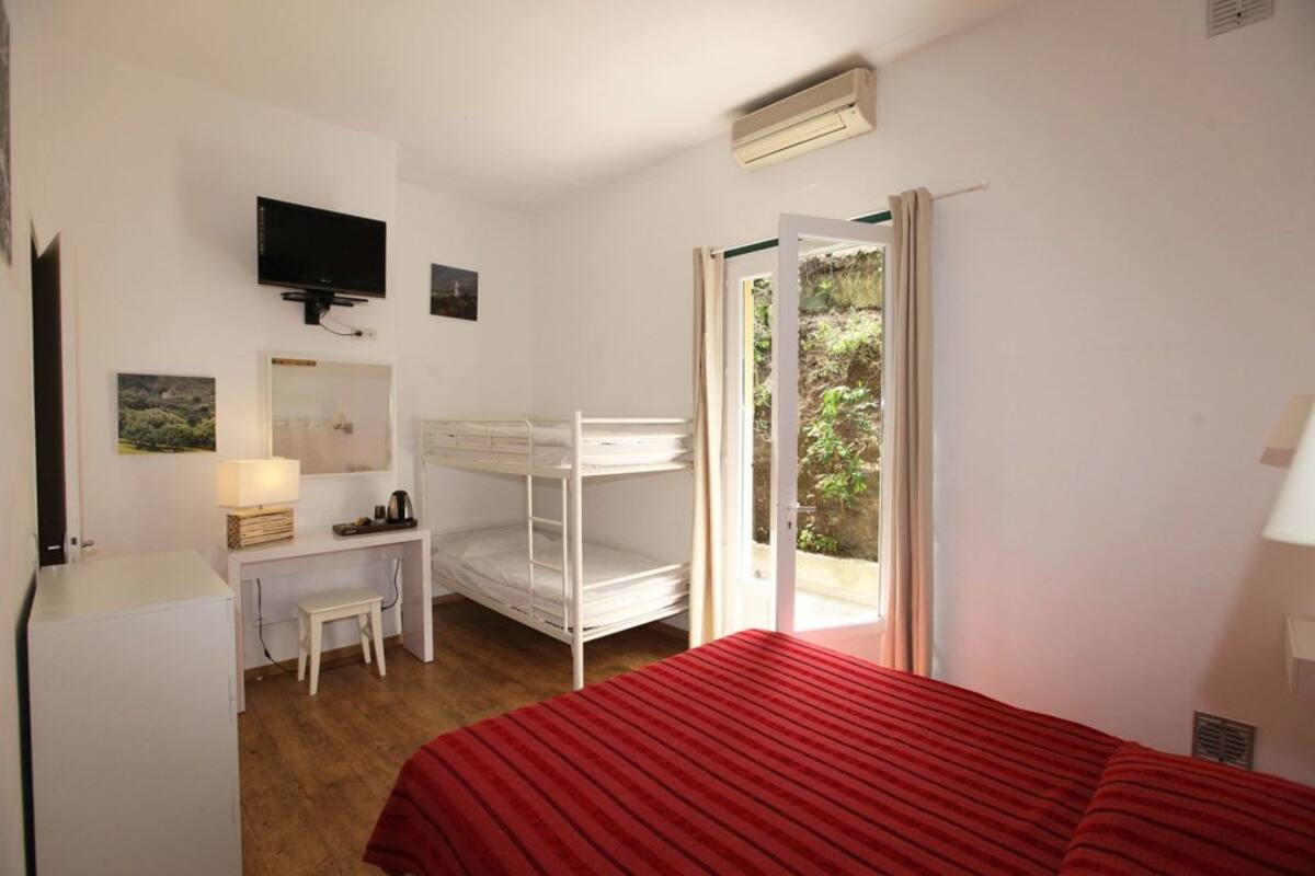 Un dormitorio con una litera, un escritorio con silla, un televisor y una ventana con vistas a zonas verdes.