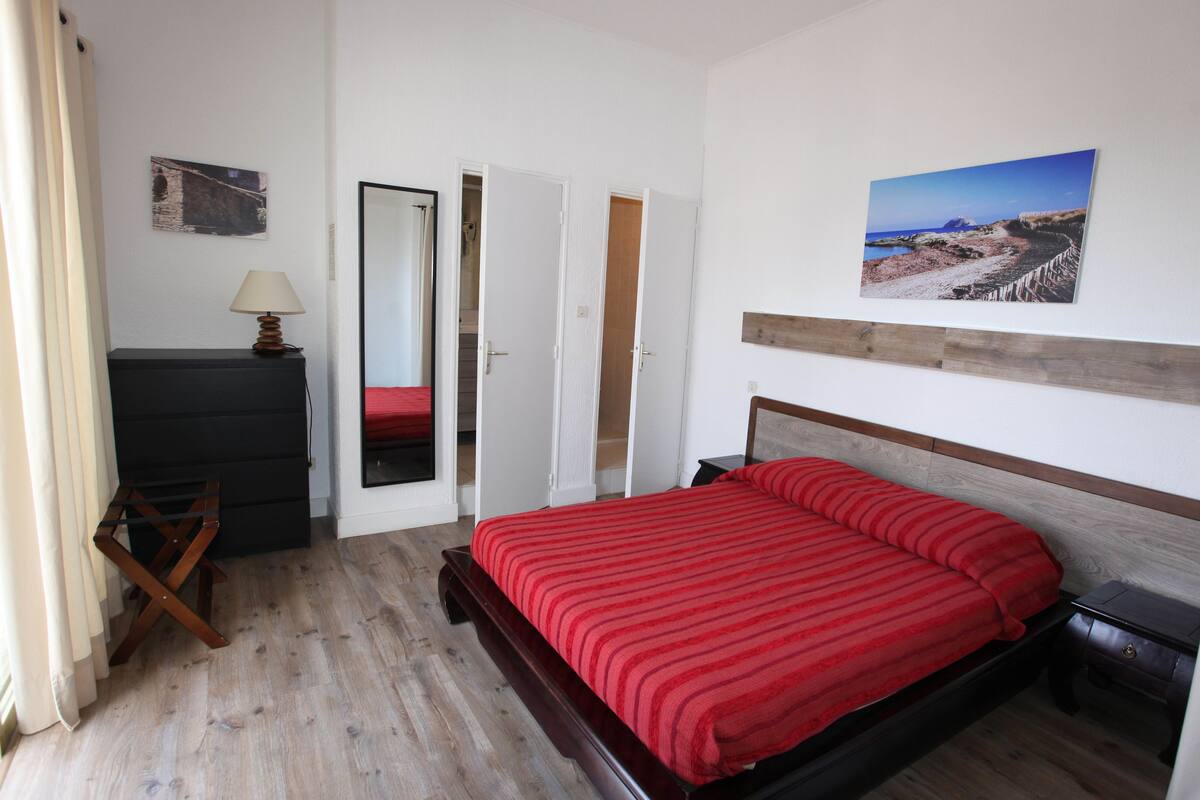 Un dormitorio con una cama de madera, una mesita de noche, un aparador, un espejo y una puerta que da a un baño.