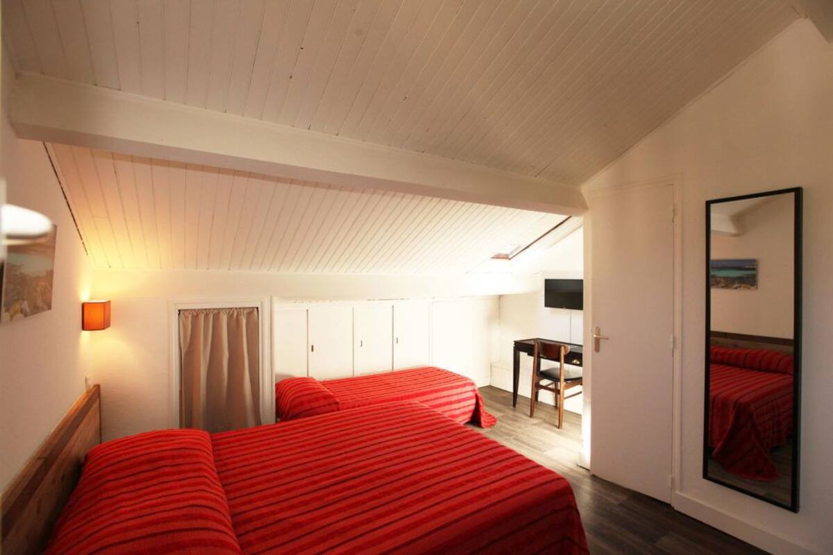 Una habitación con dos camas, un escritorio, una silla, un televisor y un espejo.