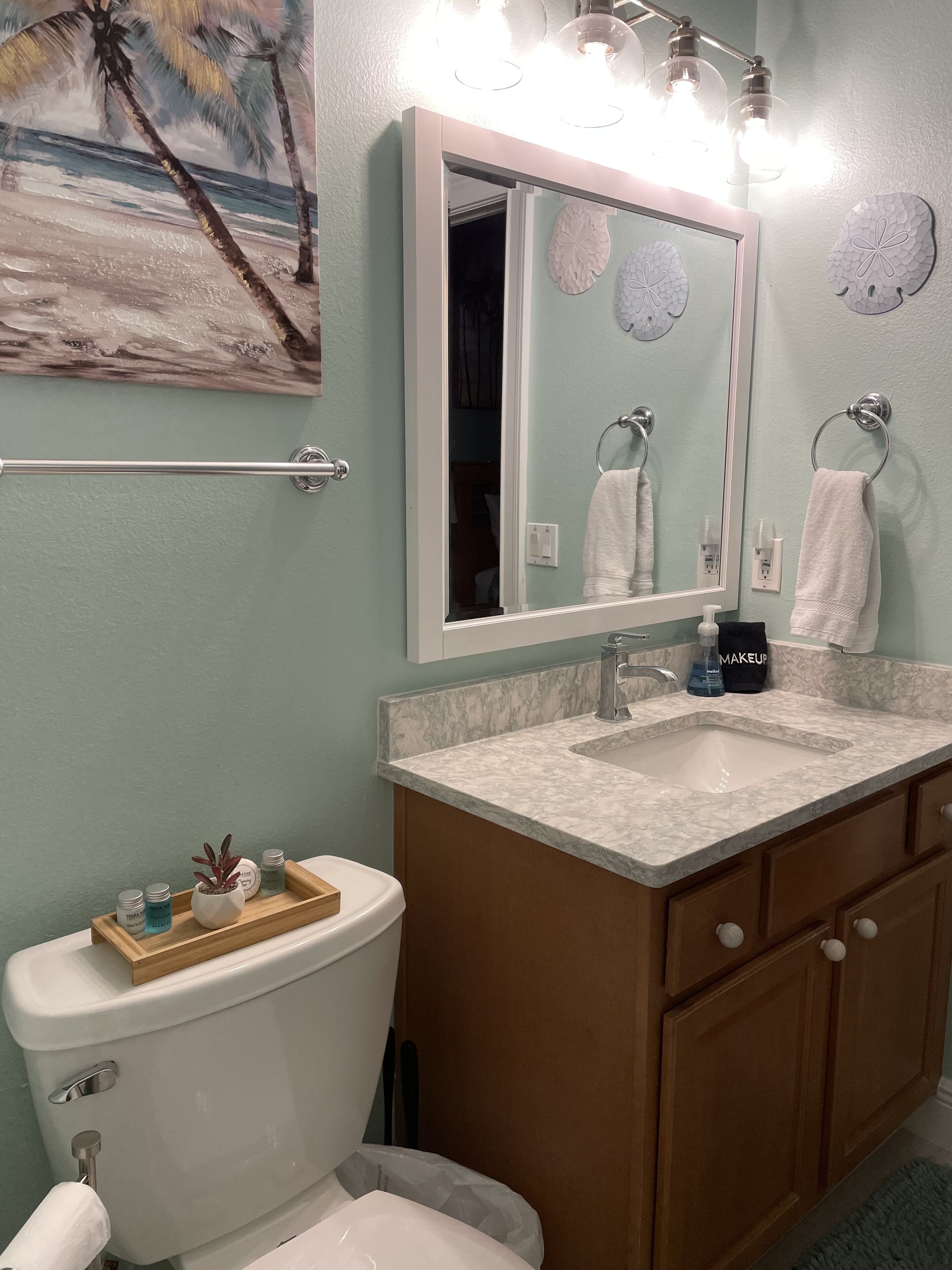 Een badkamer met toilet, wastafel en een opbergmeubel. Boven de wastafel hangt een spiegel en aan de muur zit een handdoekhouder.