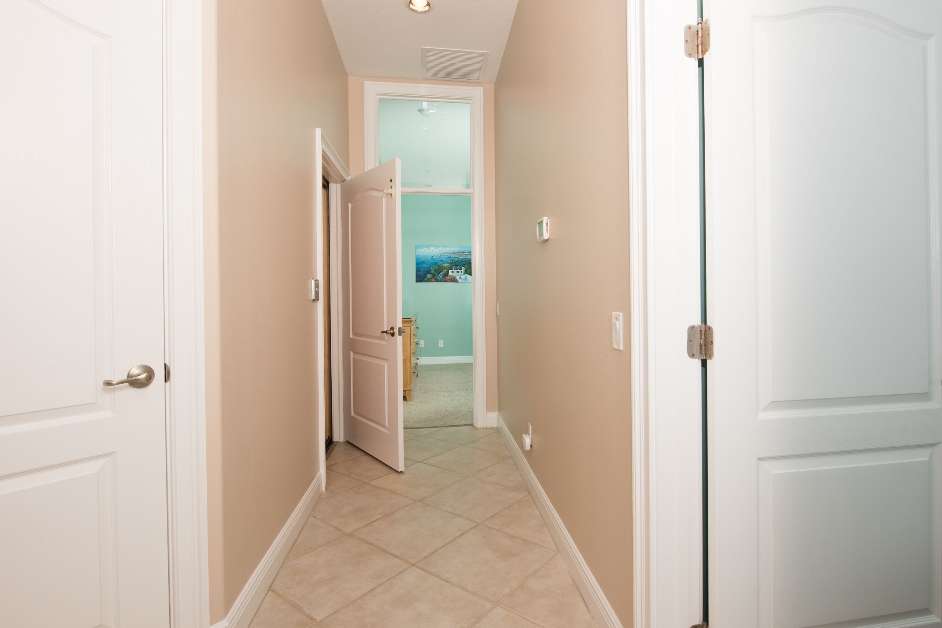 Un pasillo con paredes color beige y puertas blancas, que conduce a una habitación con vista a un paisaje a través de un ventanal.