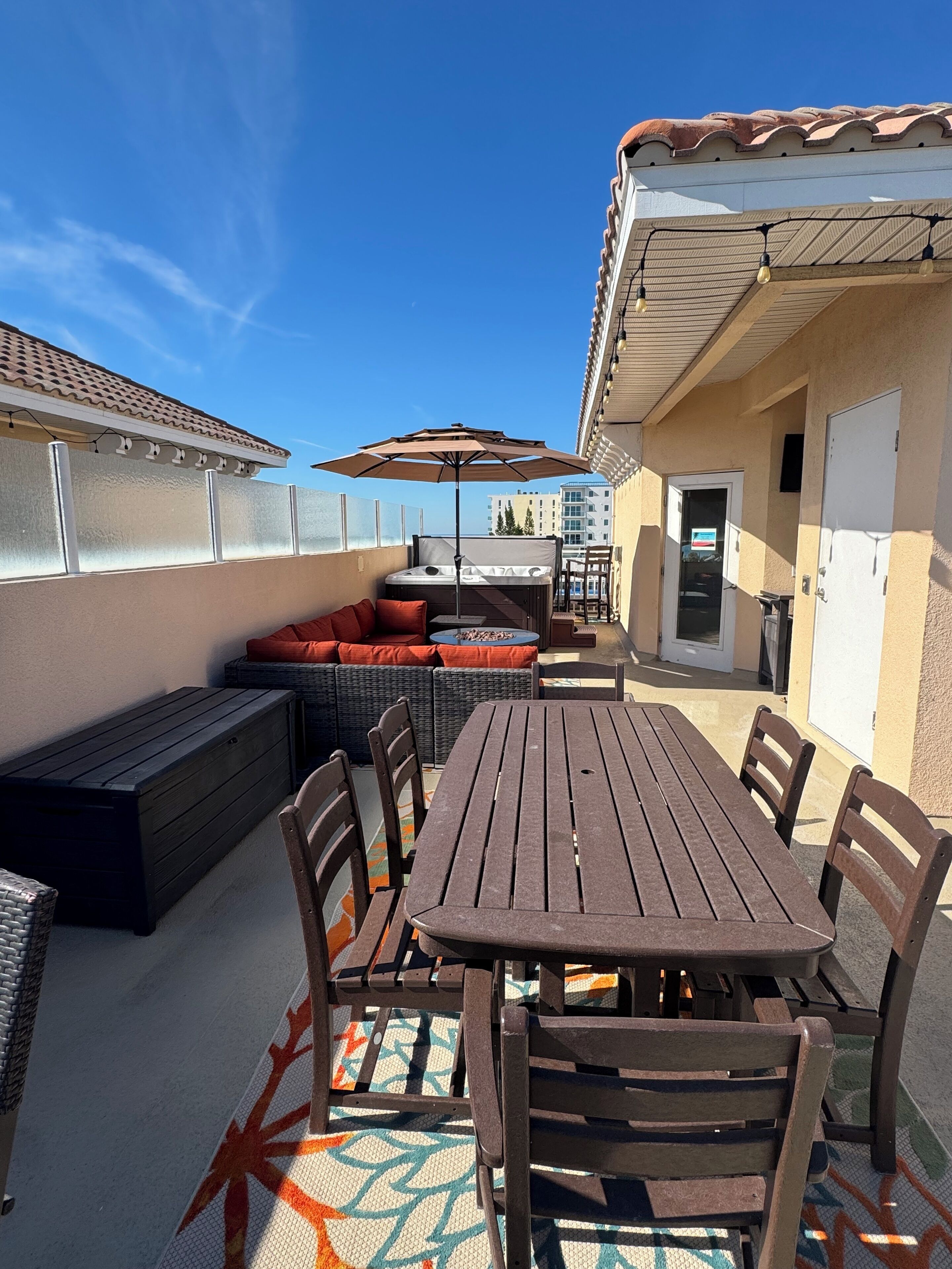 Une terrasse extérieure avec une table et des chaises en bois, un canapé avec des coussins rouges et un parasol.