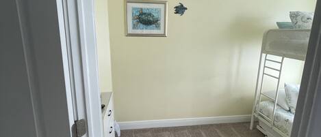A room with a beige carpet, a white door, and a bunk bed with a white frame.