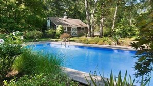 Una piscina circondata da vegetazione lussureggiante e una piccola casa sullo sfondo.