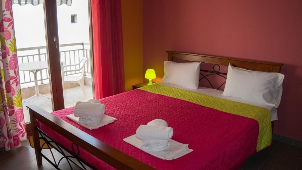 A hotel room with a bed, a nightstand, a lamp, and a view of the outside balcony.