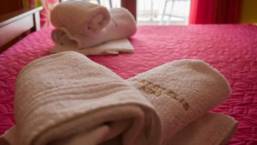 Una cama con ropa de cama rosa y toallas blancas enrolladas.