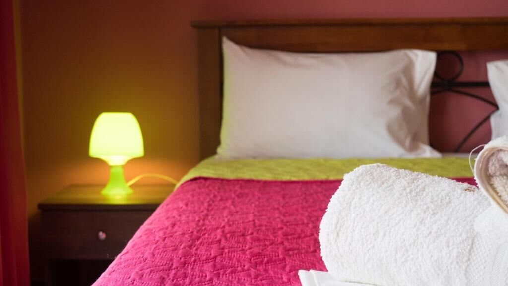 Ein Hotelzimmer mit Bett, Nachttisch mit Lampe und weißem Handtuch auf dem Bett.