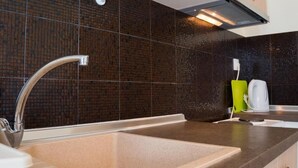 Eine moderne Küche mit einer Edelstahlspüle, einem grünen Becherhalter und einem weißen Wasserkocher auf der Arbeitsfläche.