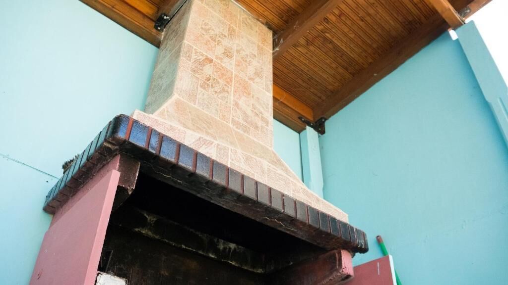 A brick chimney with a tiled top, attached to a building with a wooden ceiling and a light blue wall.