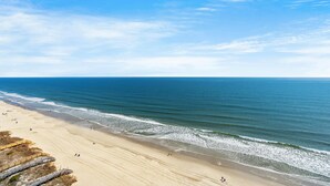 Une plage avec une promenade en bois menant au rivage, un ciel bleu clair et une mer calme.