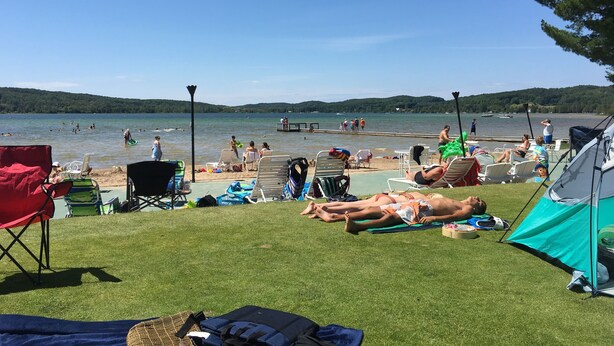 Un camping junto al lago con tiendas de campaña, sillas de jardín y un muelle.