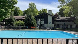 Una piscina con zona vallada, sillas de descanso y un edificio con chimenea al fondo.