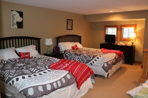 Une chambre avec deux lits, chacun agrémenté de draps et d’oreillers à motifs. On y trouve également des œuvres d’art murales et un téléviseur posé sur une commode.