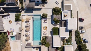 An aerial view of a modern residential area with a swimming pool, lounge chairs, and a few cars parked nearby. - Mykonos Drops (Mykonos)