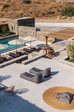 A rooftop pool area with stone walls, lounge chairs, and a wooden pergola. - Mykonos Drops (Mykonos)